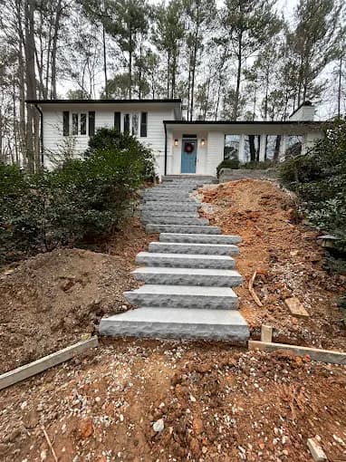 New poured concrete steps and landings forming a front walkway up the slope to a mid-century home, with the surrounding grade freshly cut and awaiting backfill.
