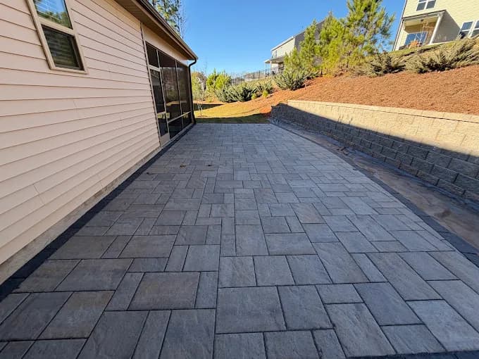 Charcoal paver walkway running the length of a house to a segmental block retaining wall that holds back a freshly graded slope of red clay.