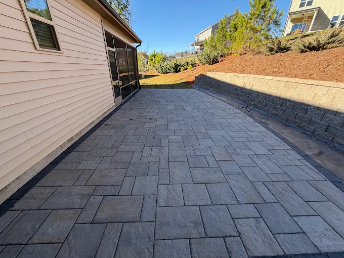 Charcoal paver walkway running the length of a house to a segmental block retaining wall that holds back a freshly graded slope of red clay.